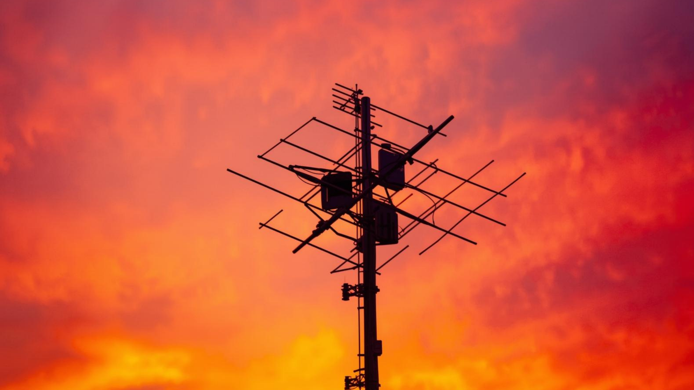 Outdoor TV antenna against a red-orange heatwave sky, illustrating heatwave TV problems and signal issues caused by extreme summer temperatures.
