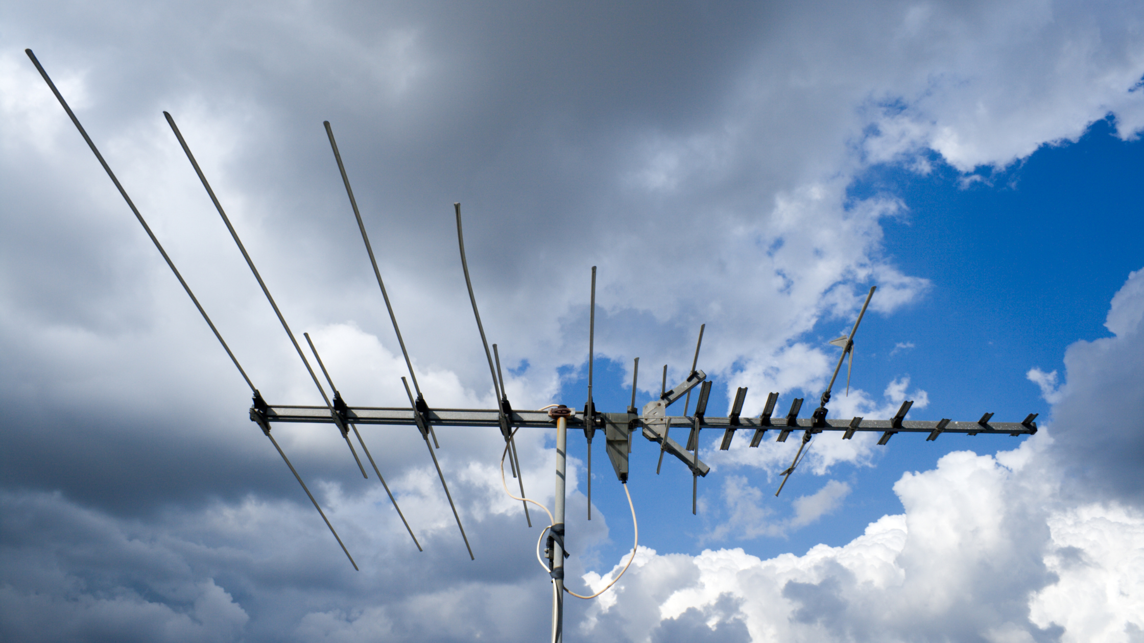 Rooftop TV antenna against cloudy sky showing exposed coaxial cable prone to antenna cable corrosion from humid weather