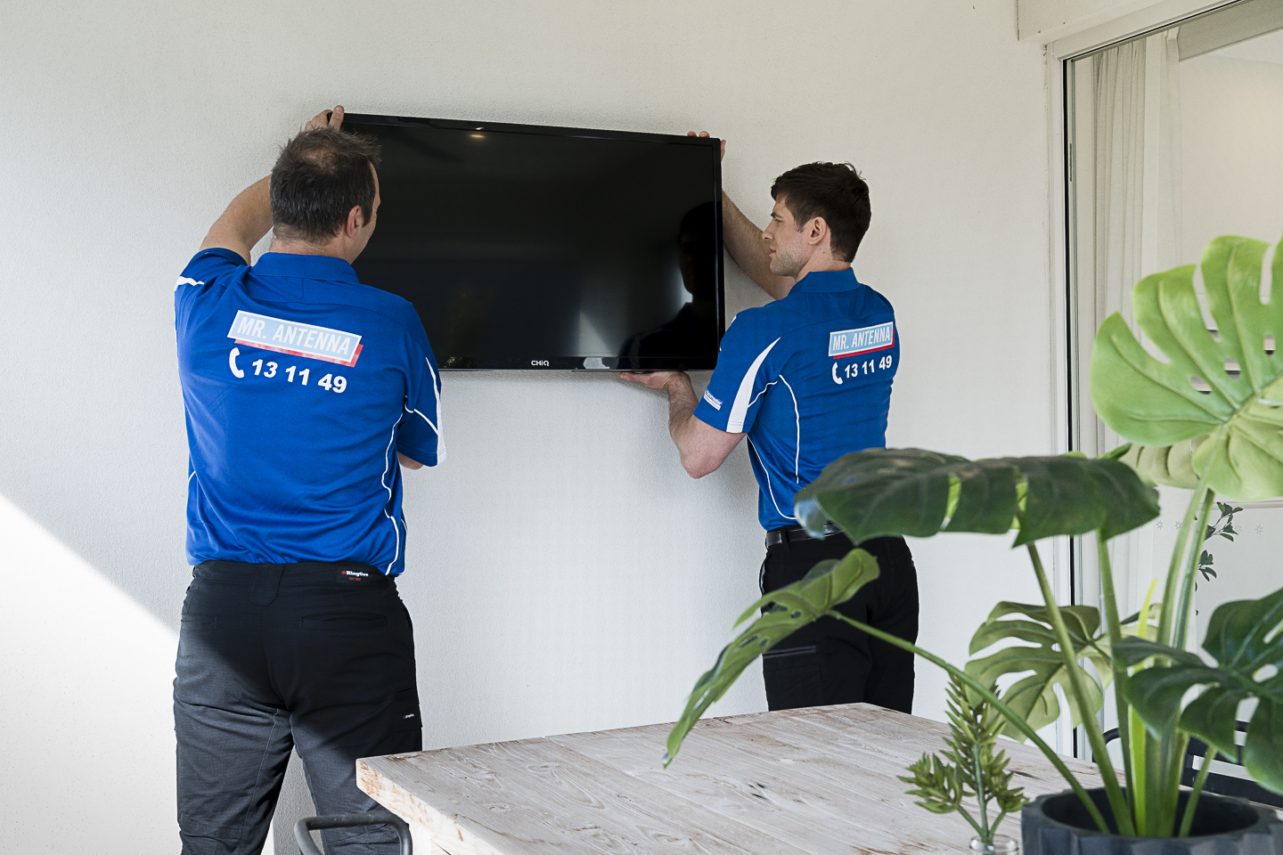 Professional antenna technicians installing a wall-mounted TV to ensure strong reception and signal quality across multiple TVs in the home