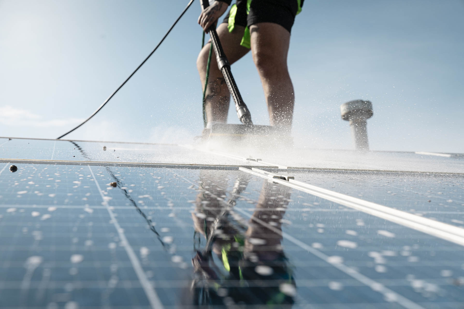 Worker cleaning solar panels on a rooftop with water and brush to improve efficiency and protect against gutter overflow and damage.