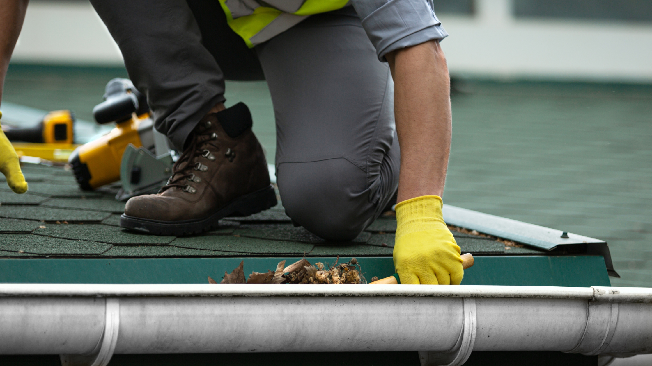 Worker manually clearing debris from a roof gutter, showing the traditional method that gutter vacuum cleaning now replaces.