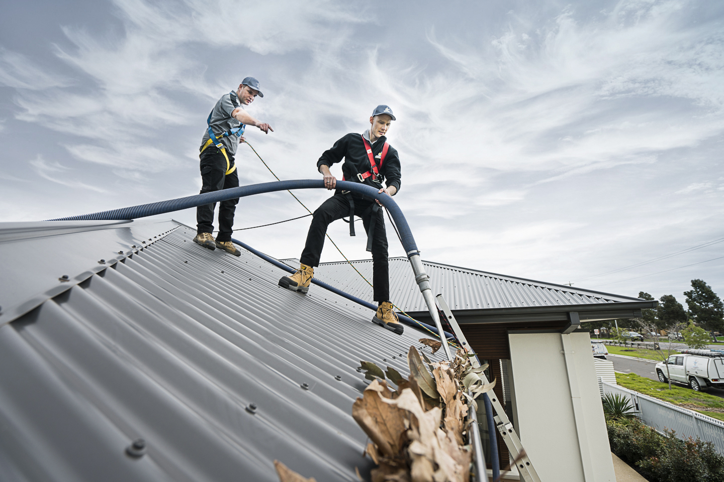Professional gutter cleaners in Melbourne using vacuum equipment to remove leaves and debris from a rooftop gutter, preventing water damage.