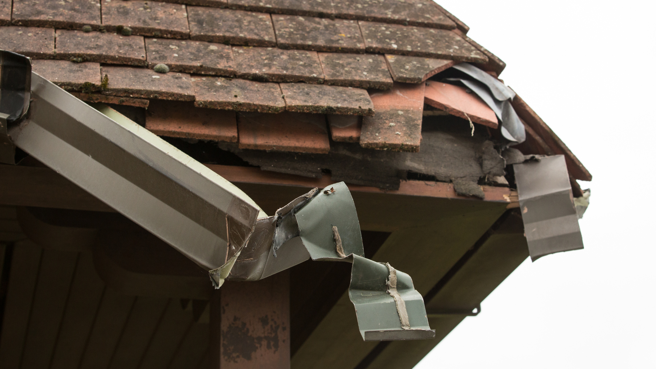Post storm gutter damage showing bent metal gutter and roof tile displacement after severe weather