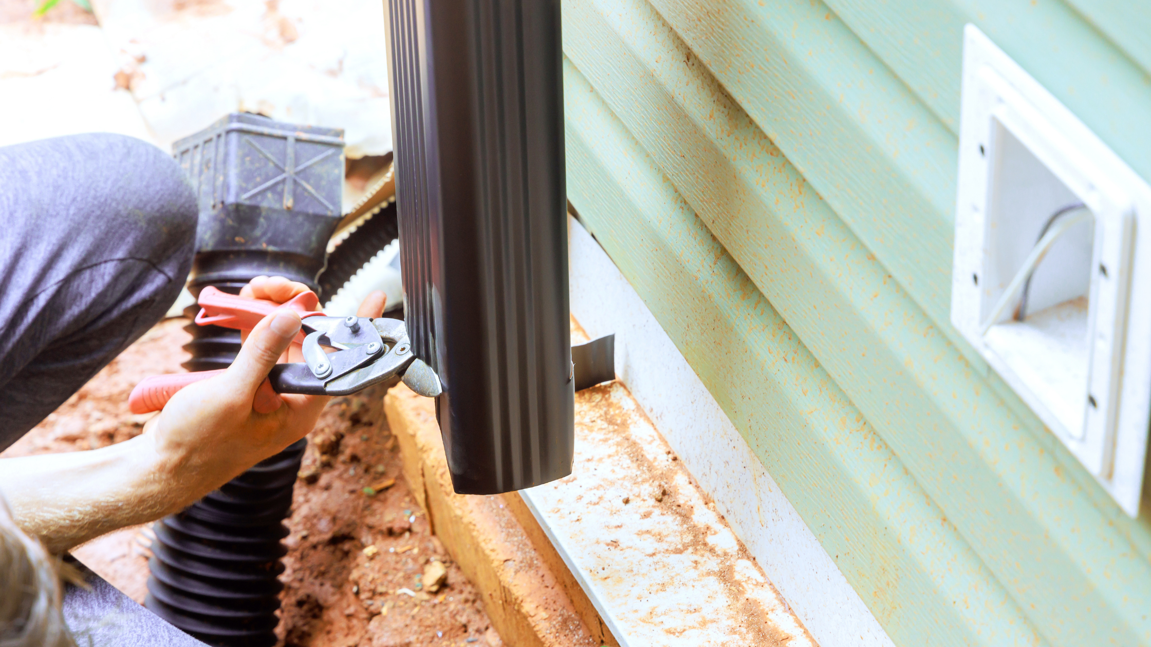 Close-up of a technician repairing a small gutter blockage near a house downpipe to prevent water damage and costly repairs