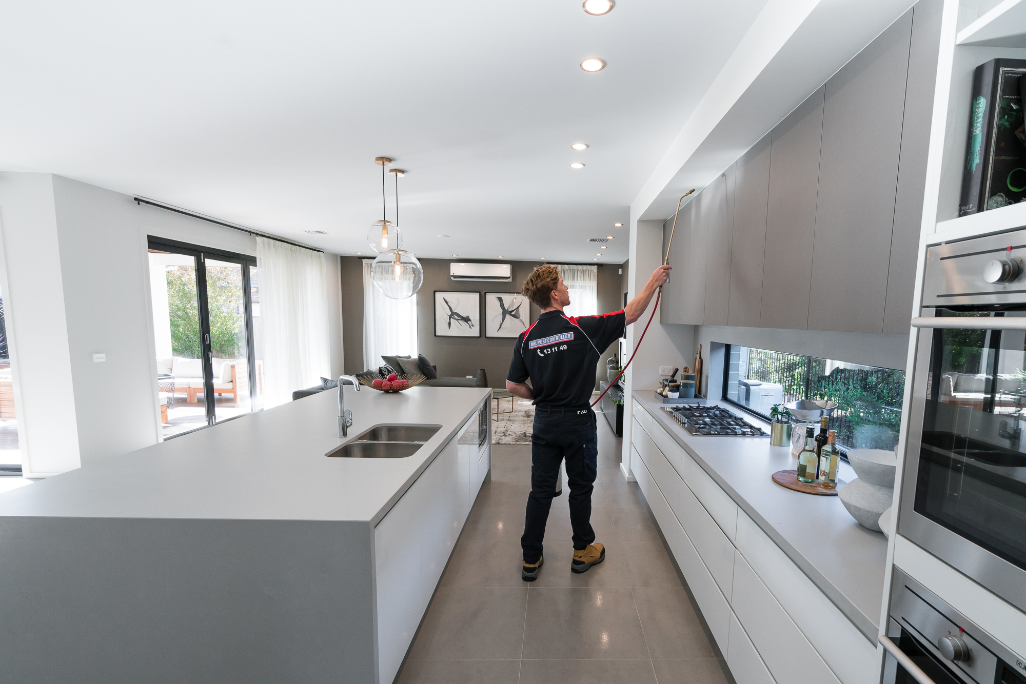 Professional apartment exterminator treating kitchen cabinets in a modern Melbourne home using pet-safe pest control methods.