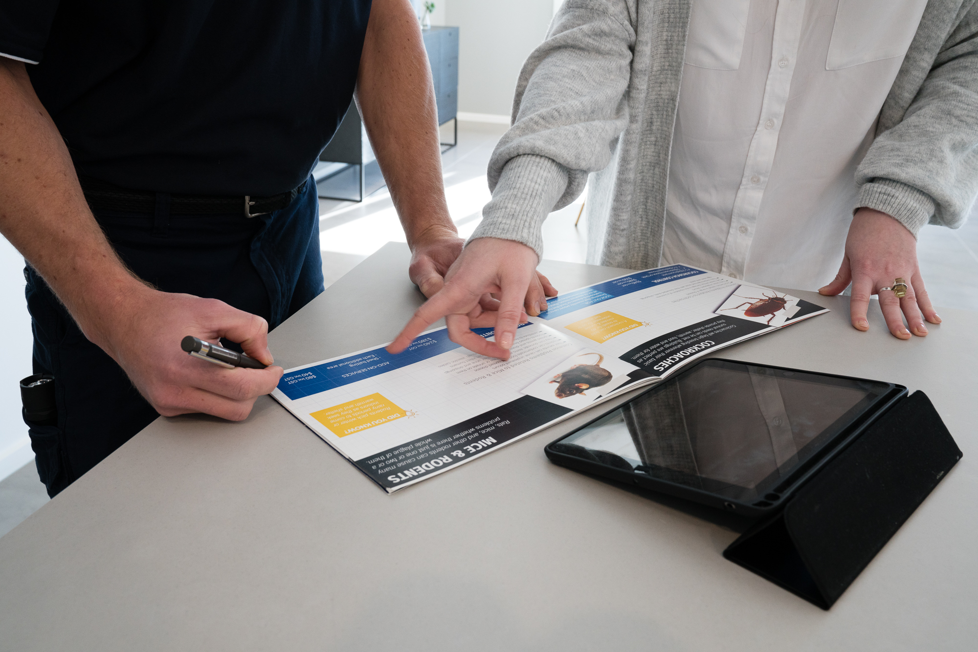 Pest control technician discussing a rodent treatment plan with a homeowner using an inspection report during a professional consultation.