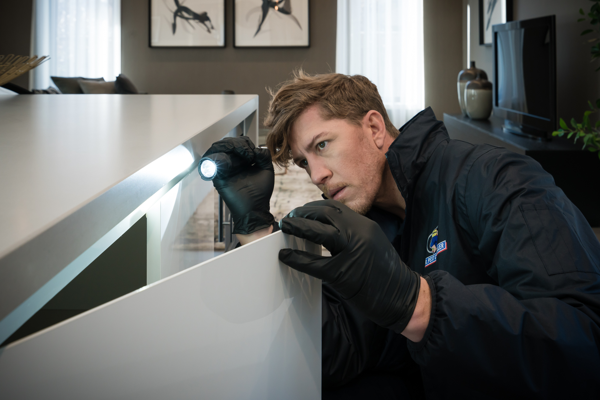 Pest control technician inspecting a kitchen cabinet with a flashlight during professional mice control in a Melbourne home.